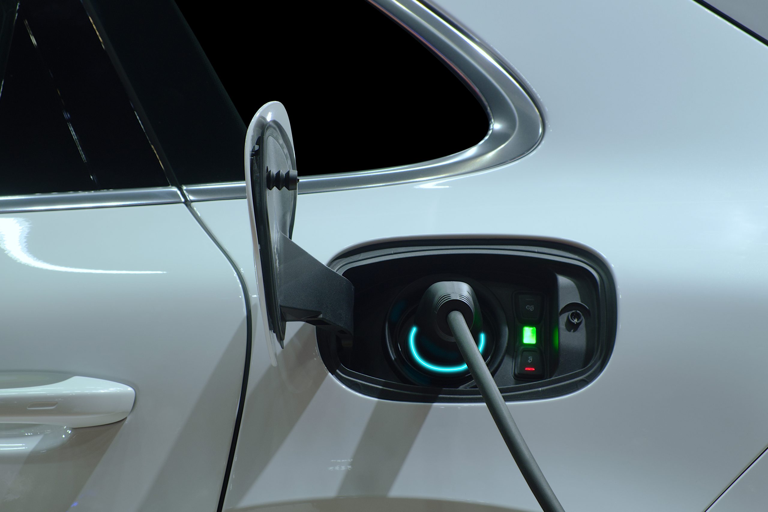 Close-up hand grip plug of industrial electric charging machine connected with socket charge on white electric car for rechargeable battery, zero emission vehicle and green energy for smart life